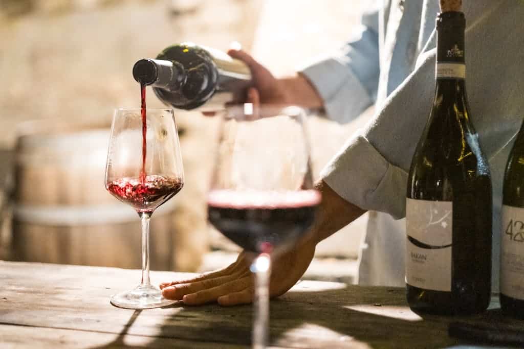 Wine being poured into a glass at a lakeside setting.