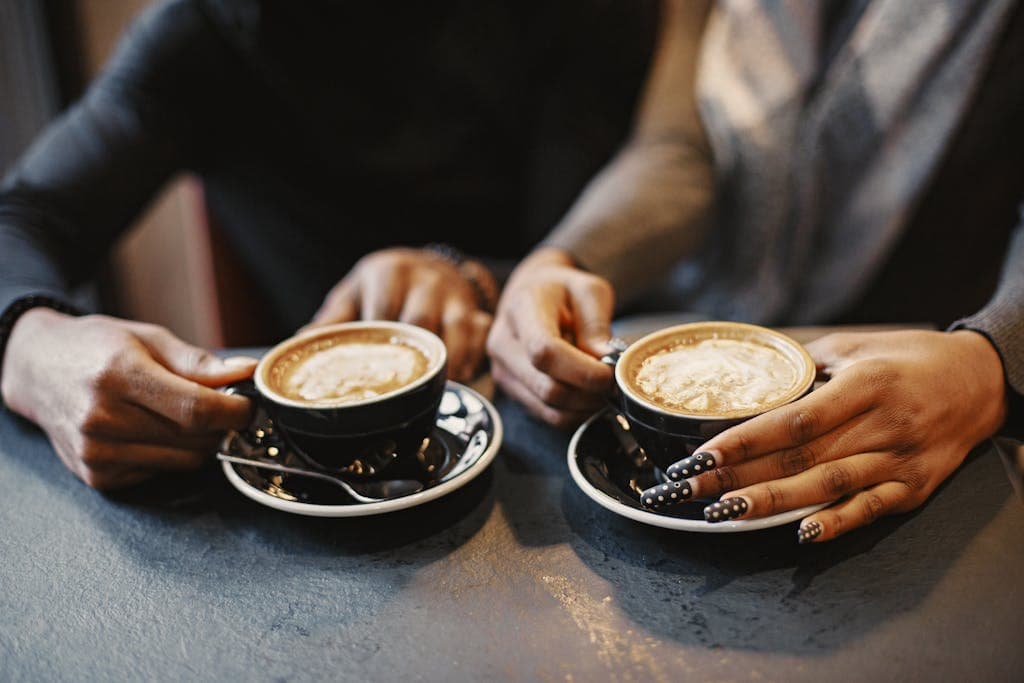 Two people holding cups of coffee at the lake, enjoying a relaxing moment.