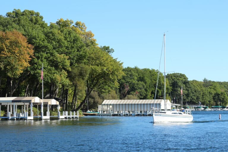 Scenic Lake Geneva scene featuring sailboats, docks, and vibrant fall foliage on a clear day.