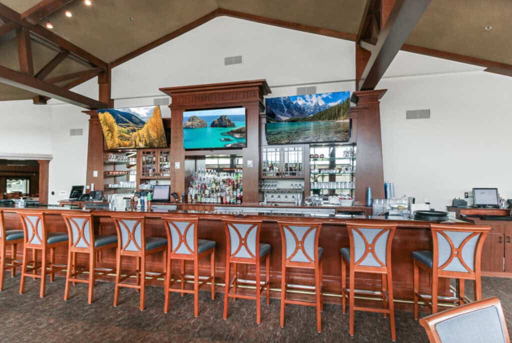 Indoor bar at Lake Geneva with scenic mountain views on multiple screens.