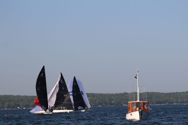 Sailing boats racing on Lake Geneva with a small motorboat nearby under clear blue skies.