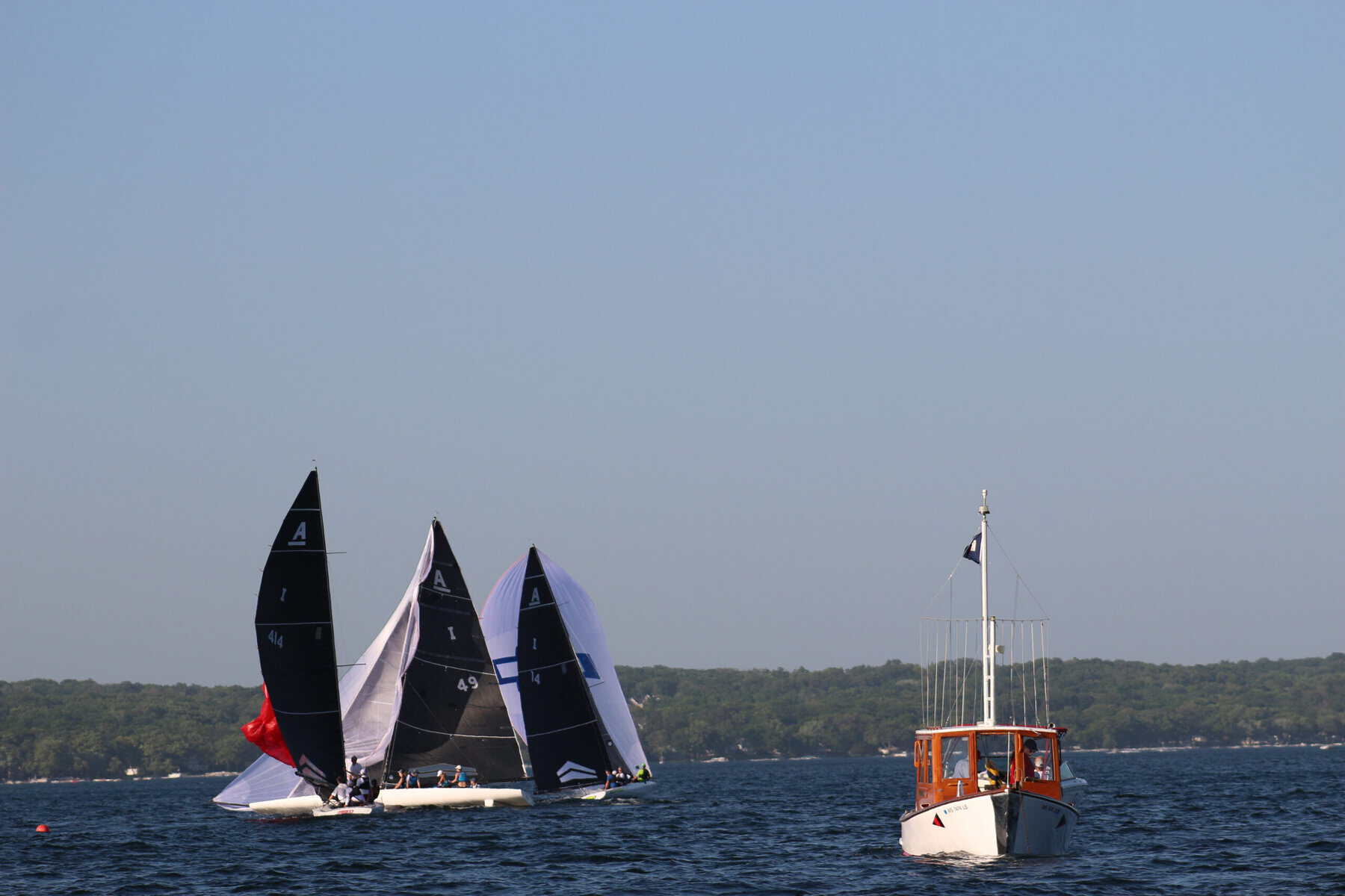 Sailing boats racing on Lake Geneva with a small motorboat nearby under clear blue skies.