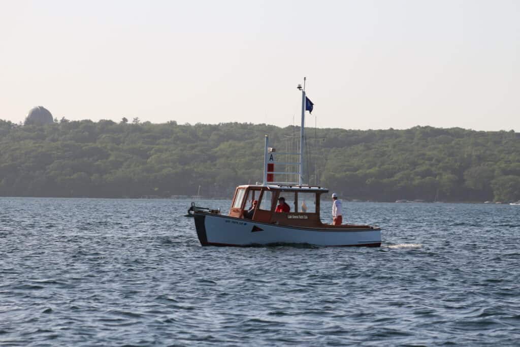 Small boat on Lake Geneva with a forested shoreline in the background.