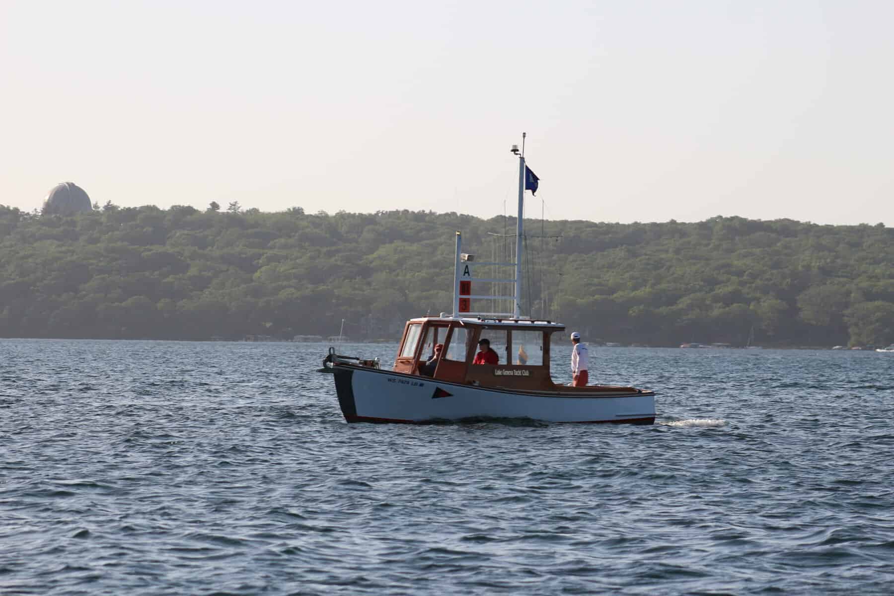 Small boat on Lake Geneva with a forested shoreline in the background.