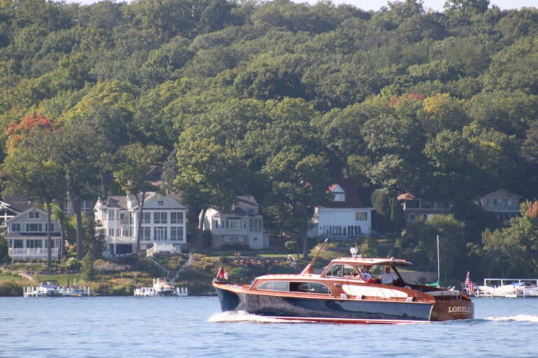 Luxury yacht cruising on Lake Geneva with lakeside homes in background.