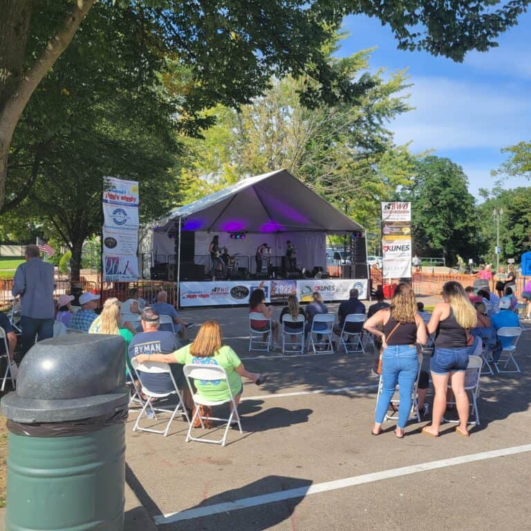 Outdoor live music performance at Lake Geneva with audience and stage under trees.