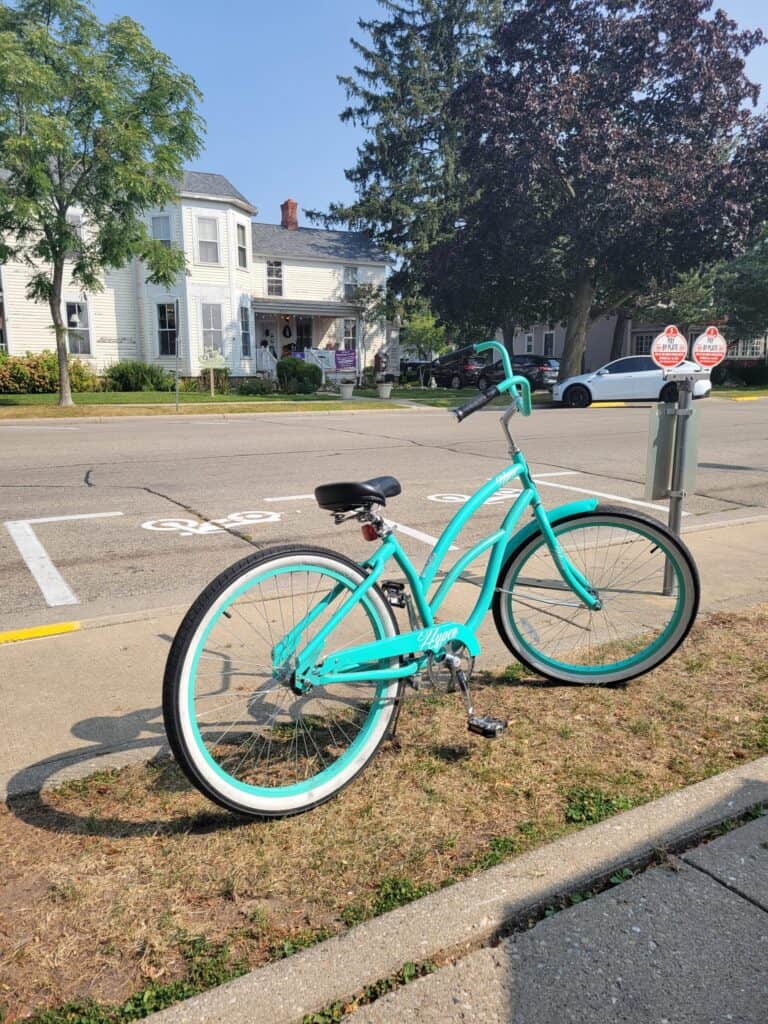 Bright turquoise bicycle parked on sidewalk near historic house.