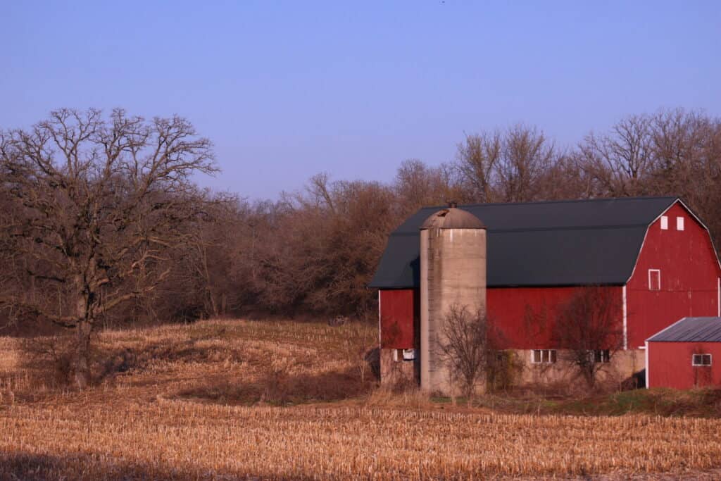 Red barn with silo and trees in a rural landscape near Lake Geneva.