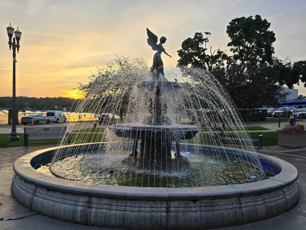 Scenic fountain with angel sculpture at Lake Geneva during sunset.