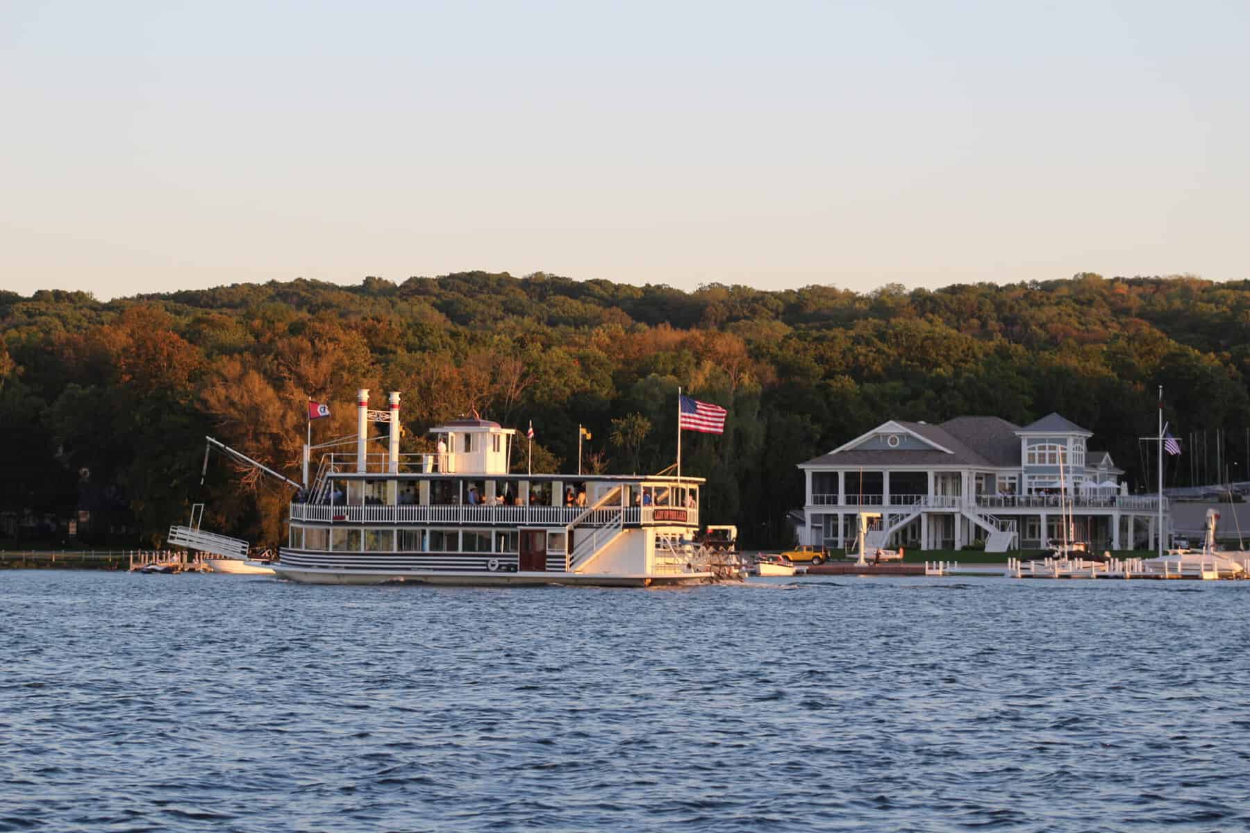 The Lady of the Lake paddlewheeler in evening light, passing a lakefront yacht club on Geneva Lake