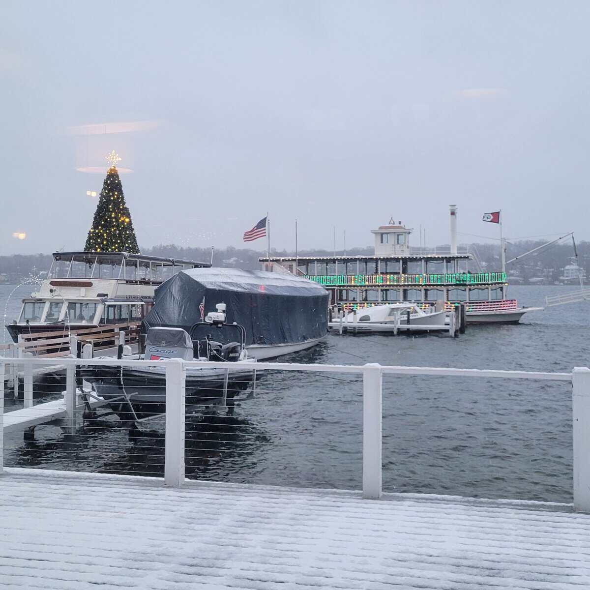 Lake Geneva Cruise Line paddlewheeler strung with holiday lights beside a lit Christmas tree at the Riviera docks in snow