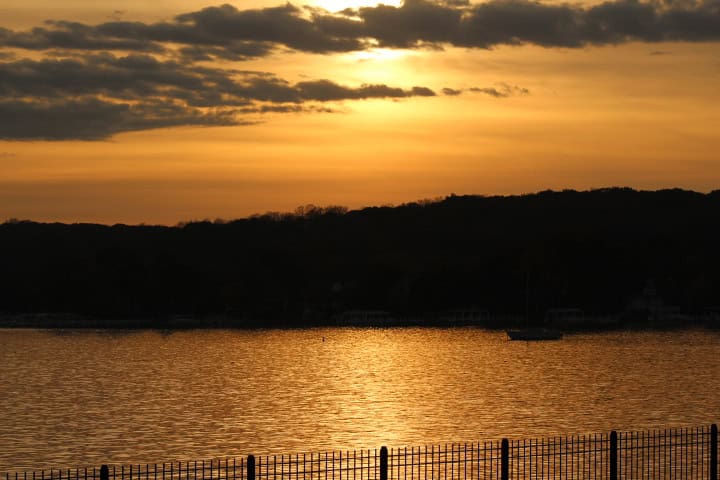 Golden sunset over calm lake with silhouetted hills and railing in foreground.