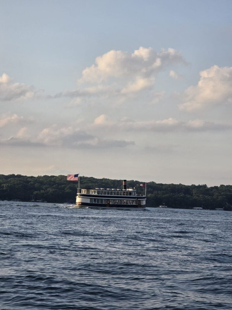 Passenger boat sailing on Lake Geneva with scenic shoreline and cloudy sky.