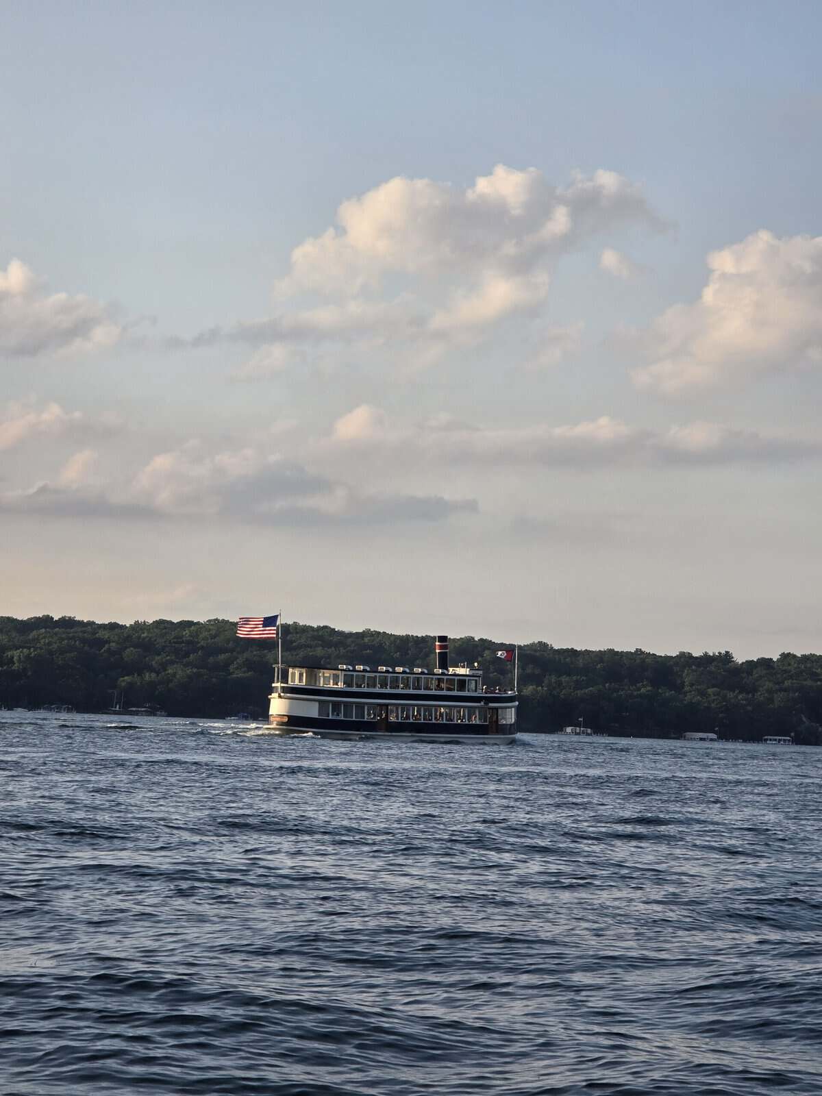 Passenger boat sailing on Lake Geneva with scenic shoreline and cloudy sky.