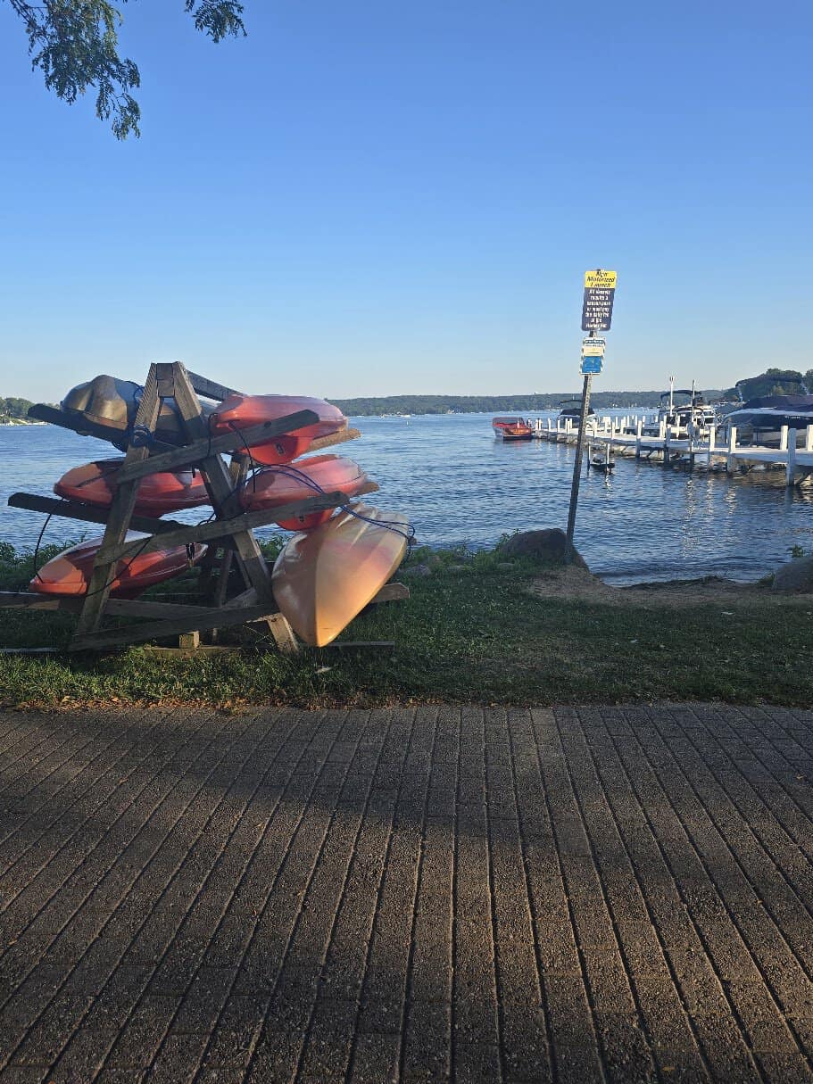 Stacked kayaks on a rack near a calm lake with a dock in the background.