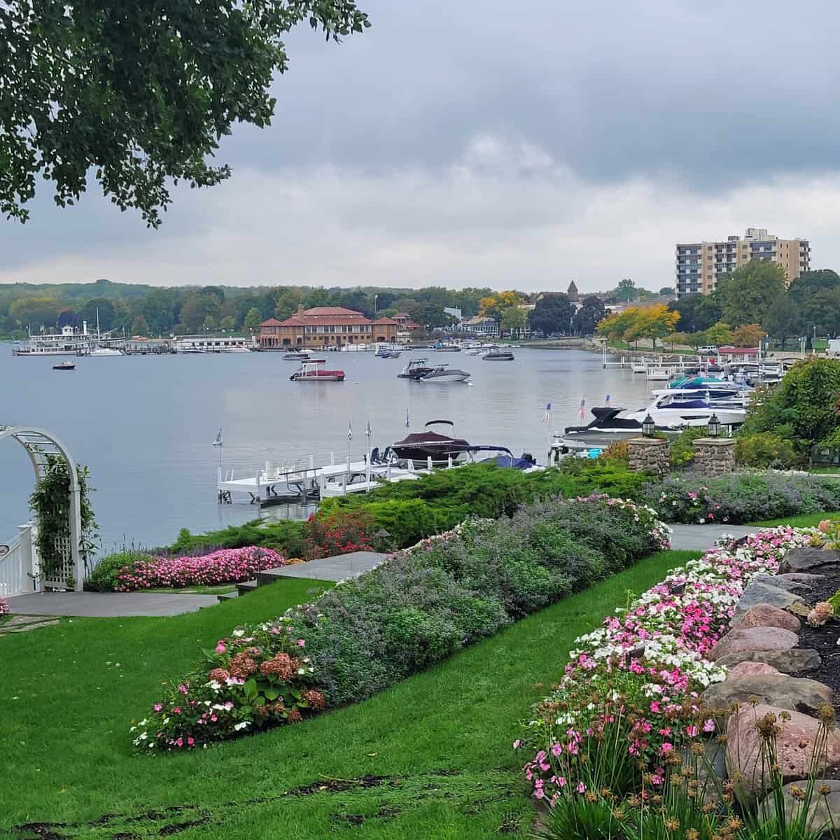 Scenic view of Lake Geneva with boats, lush gardens, and cityscape in the background.